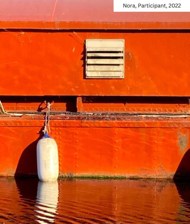 Vibrant red-orange canal boat with buoy at From Lens to Self workshop. Nora's 2022 image symbolizes self-exploration journey in Gianpietro Pucciariello's London photography coaching. Creative breakthroughs through visual storytelling.